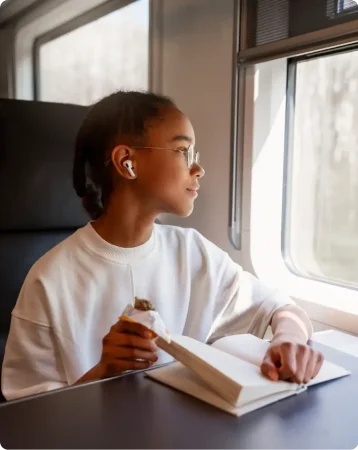 teenage girl on the train with a book, looking out the window